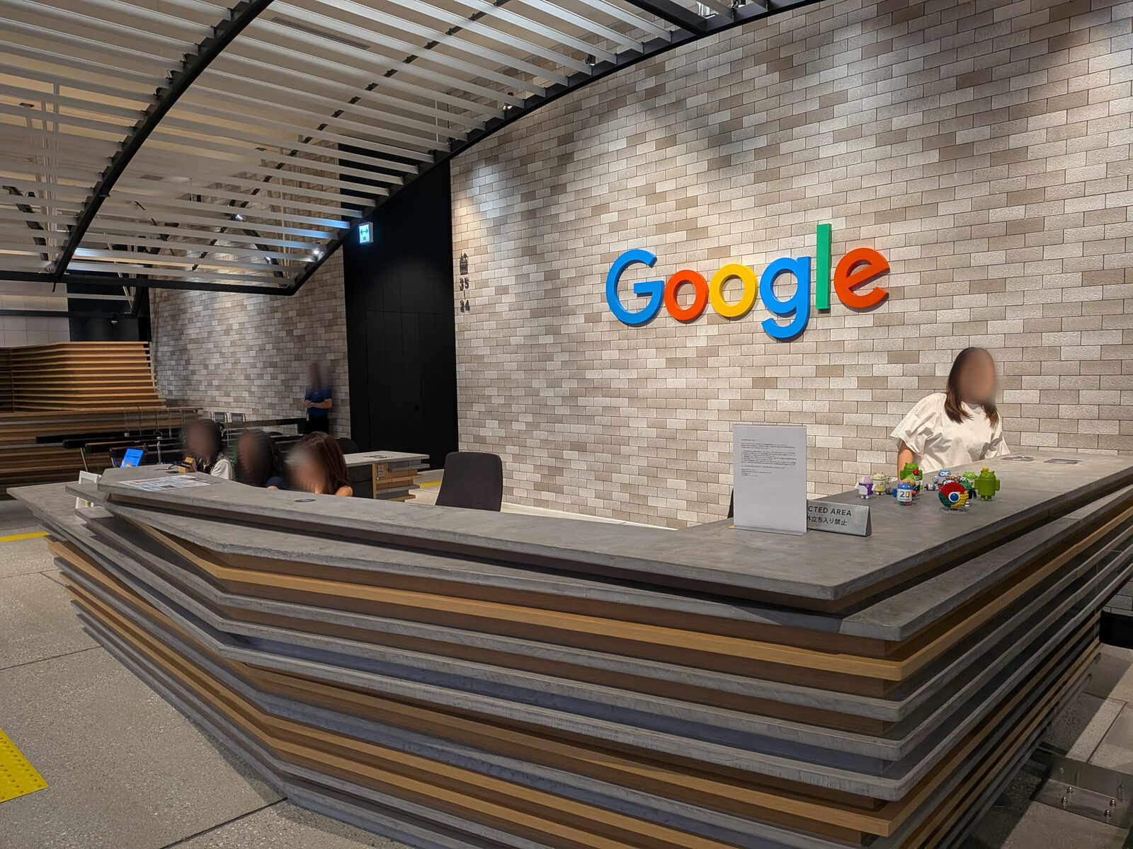 Googleオフィスの受付カウンターと、レンガ壁に掲げられたカラフルなGoogleのロゴ