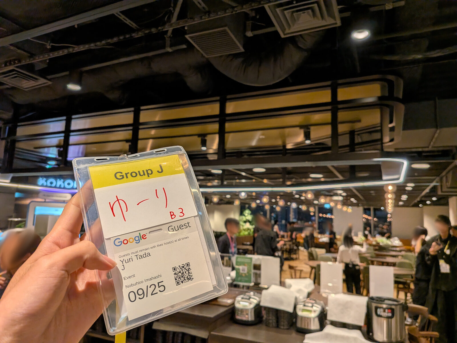 「Group J ゆーり」と書かれたGoogleのゲスト用ネームタグを手に持っている様子。奥には会場となったカフェスペースが広がる